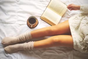 Woman's legs next to a cup of coffee and a book in bed