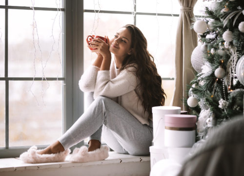 Woman with a cup of coffee sitting near a Christmas tree